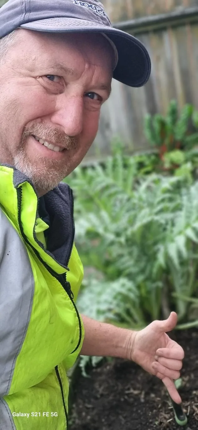 Richard Hurst, owner of RNH Lawn Care & Services, in hi-vis beside a vege garden in Tawa
