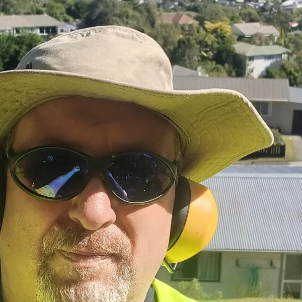 Richard Hurst of RNH Lawn Care & Services in a bucket hat and ear muffs above the houses of Tawa